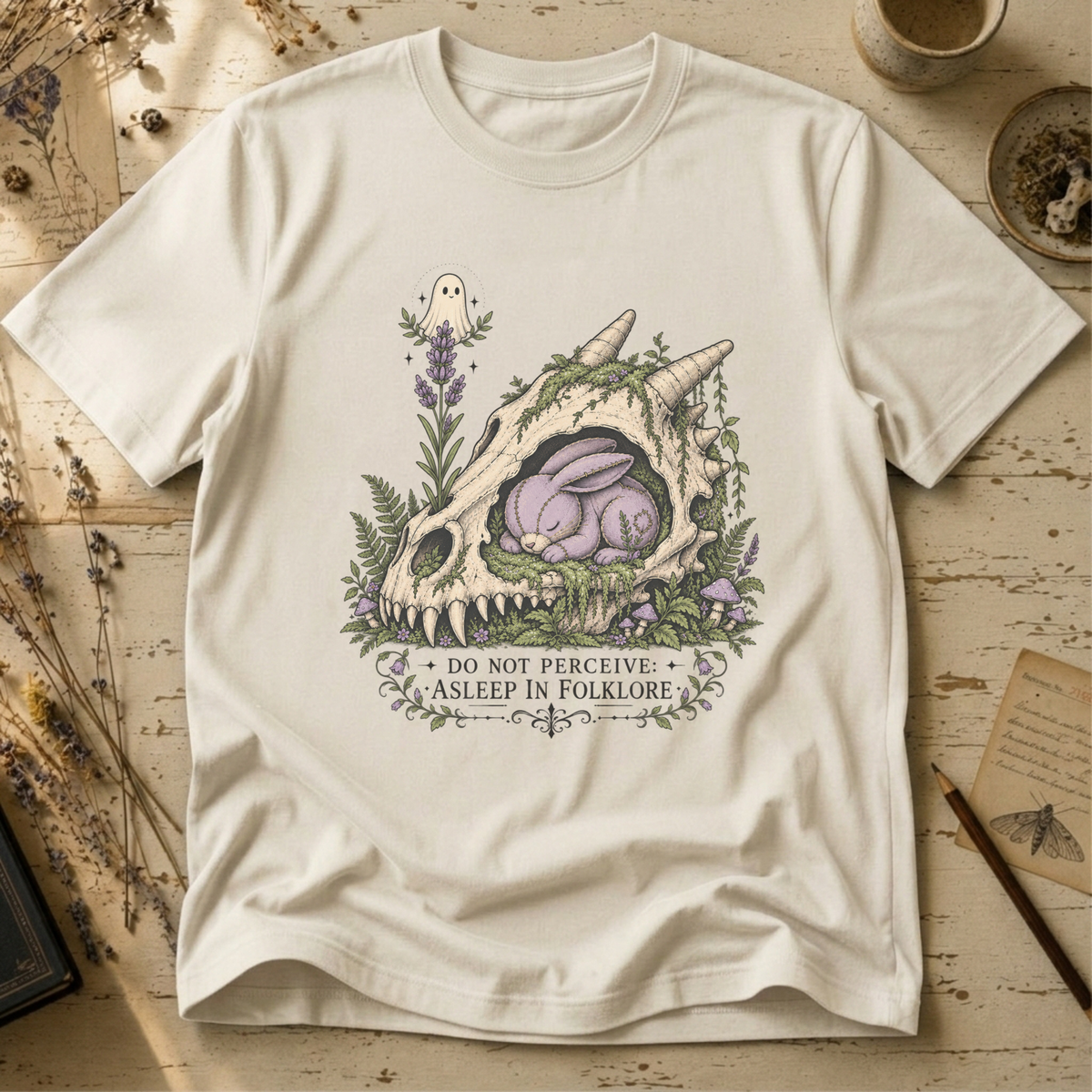 Vintage white t-shirt with an illustration of a horned, fanged skull overgrown with moss and lavender, a sleeping purple stitched rabbit curled inside it, and a small ghost hovering above.