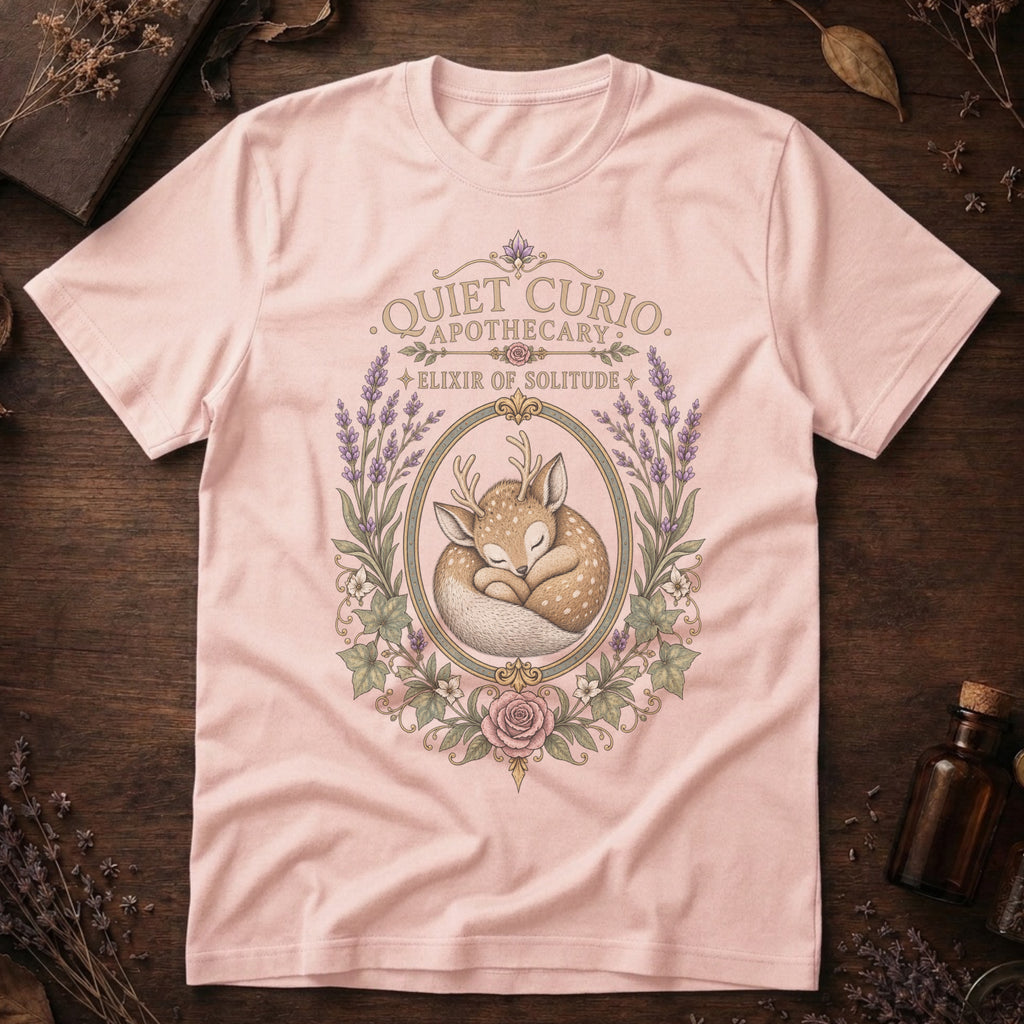 Soft pink t-shirt with a vintage apothecary label design: a sleeping fawn with white spots framed in an oval of lavender sprigs and a pink rose, labeled 'Elixir of Solitude'.