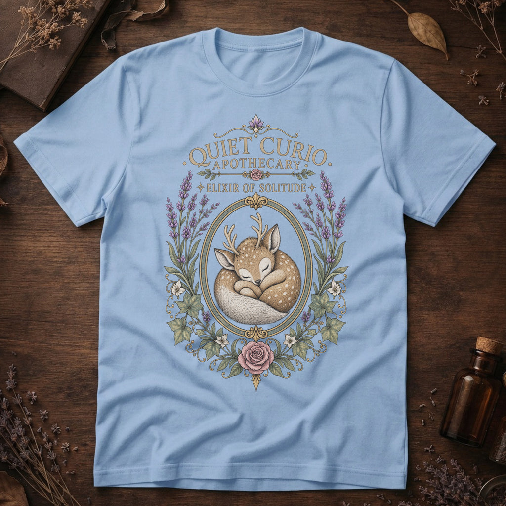 Baby blue t-shirt with a vintage apothecary label design: a sleeping fawn with white spots framed in an oval of lavender sprigs and a pink rose, labeled 'Elixir of Solitude'.