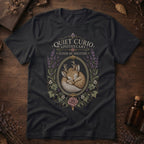 Vintage black t-shirt with a vintage apothecary label design: a sleeping fawn with white spots framed in an oval of lavender sprigs and a pink rose, labeled 'Elixir of Solitude'.