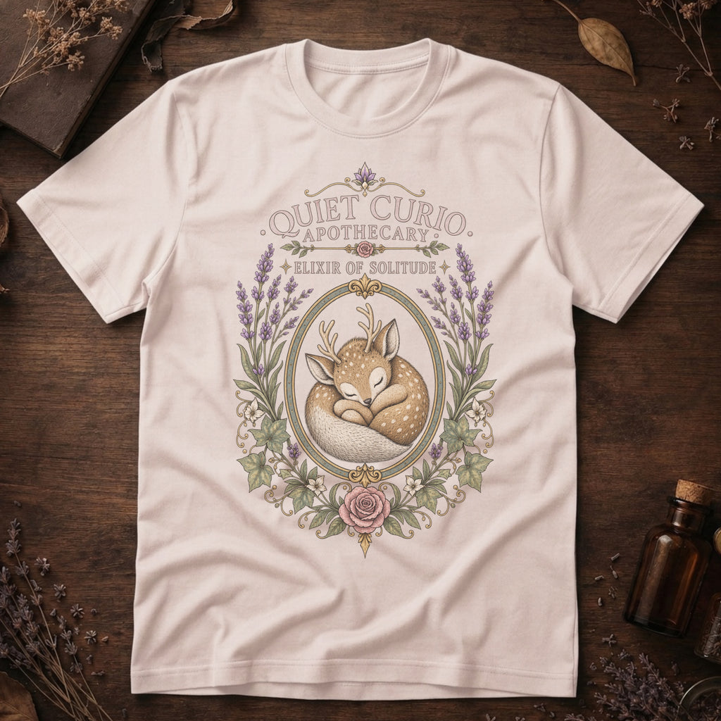 Vintage white t-shirt with a vintage apothecary label design: a sleeping fawn with white spots framed in an oval of lavender sprigs and a pink rose, labeled 'Elixir of Solitude'.