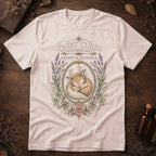 Vintage white t-shirt with a vintage apothecary label design: a sleeping fawn with white spots framed in an oval of lavender sprigs and a pink rose, labeled 'Elixir of Solitude'.