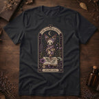 Vintage black t-shirt with a gothic herbarium illustration: a skull-shaped plant sprouting purple and pink flowers above an open botanical book, framed in an arch with a crescent moon.