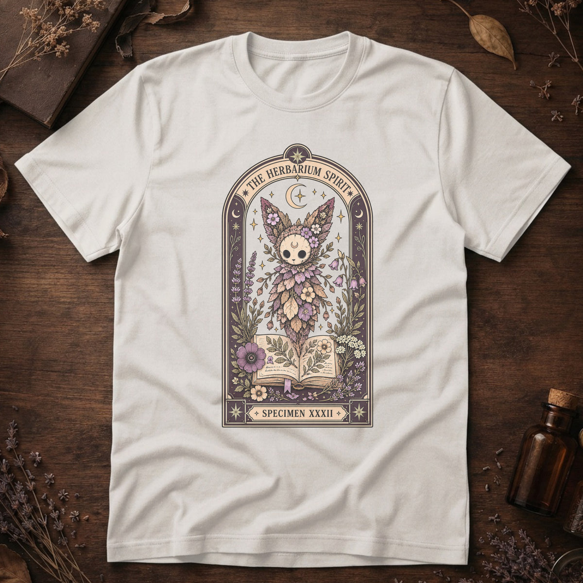Vintage white t-shirt with a gothic herbarium illustration: a skull-shaped plant sprouting purple and pink flowers above an open botanical book, framed in an arch with a crescent moon.