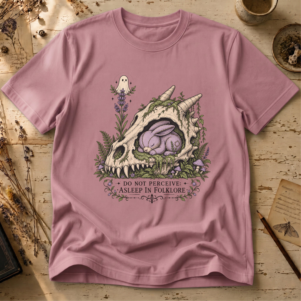 Orchid pink t-shirt with an illustration of a horned, fanged skull overgrown with moss and lavender, a sleeping purple stitched rabbit curled inside it, and a small ghost hovering above.