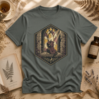 Sage green t-shirt with a stained-glass window illustration of a small hooded spirit sitting before a Gothic arched window in yellow, purple, and blue glass panels.