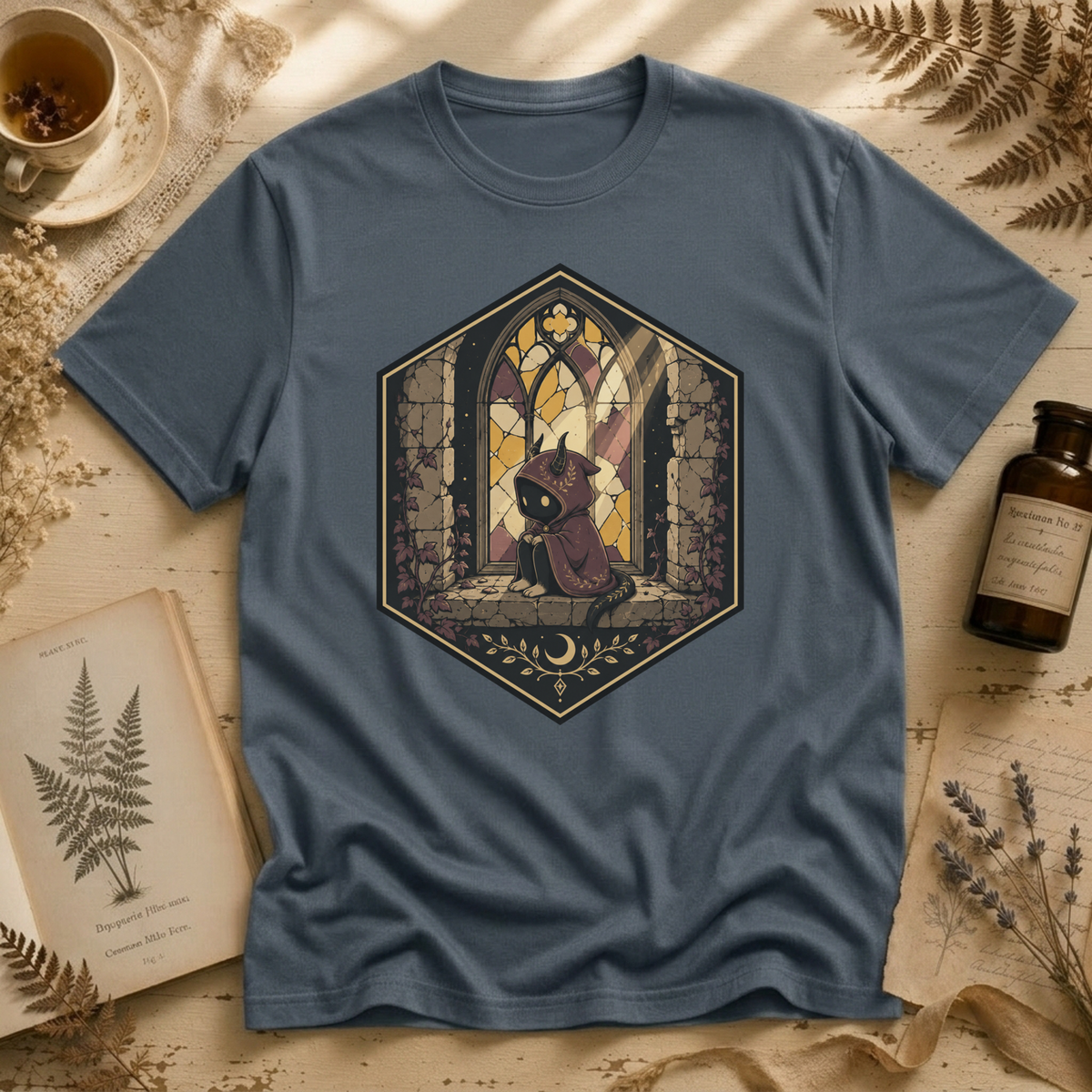 Steel blue t-shirt with a stained-glass window illustration of a small hooded spirit sitting before a Gothic arched window in yellow, purple, and blue glass panels.