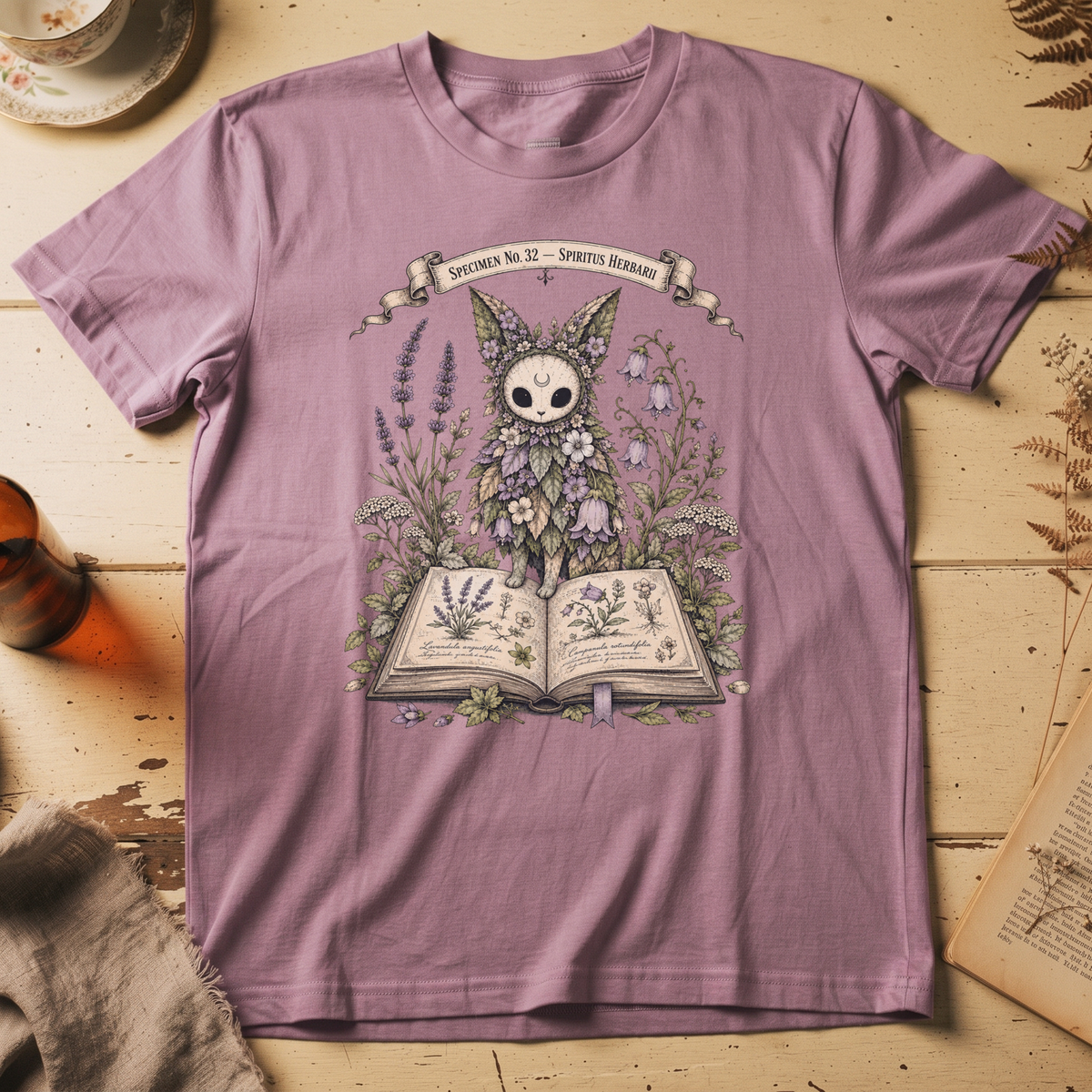 Orchid pink t-shirt with a botanical illustration of a skull-faced spirit wearing a floral crown, standing among lavender and bluebell flowers between two open books.