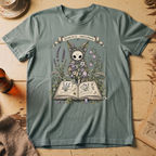 Sage green t-shirt with a botanical illustration of a skull-faced spirit wearing a floral crown, standing among lavender and bluebell flowers between two open books.