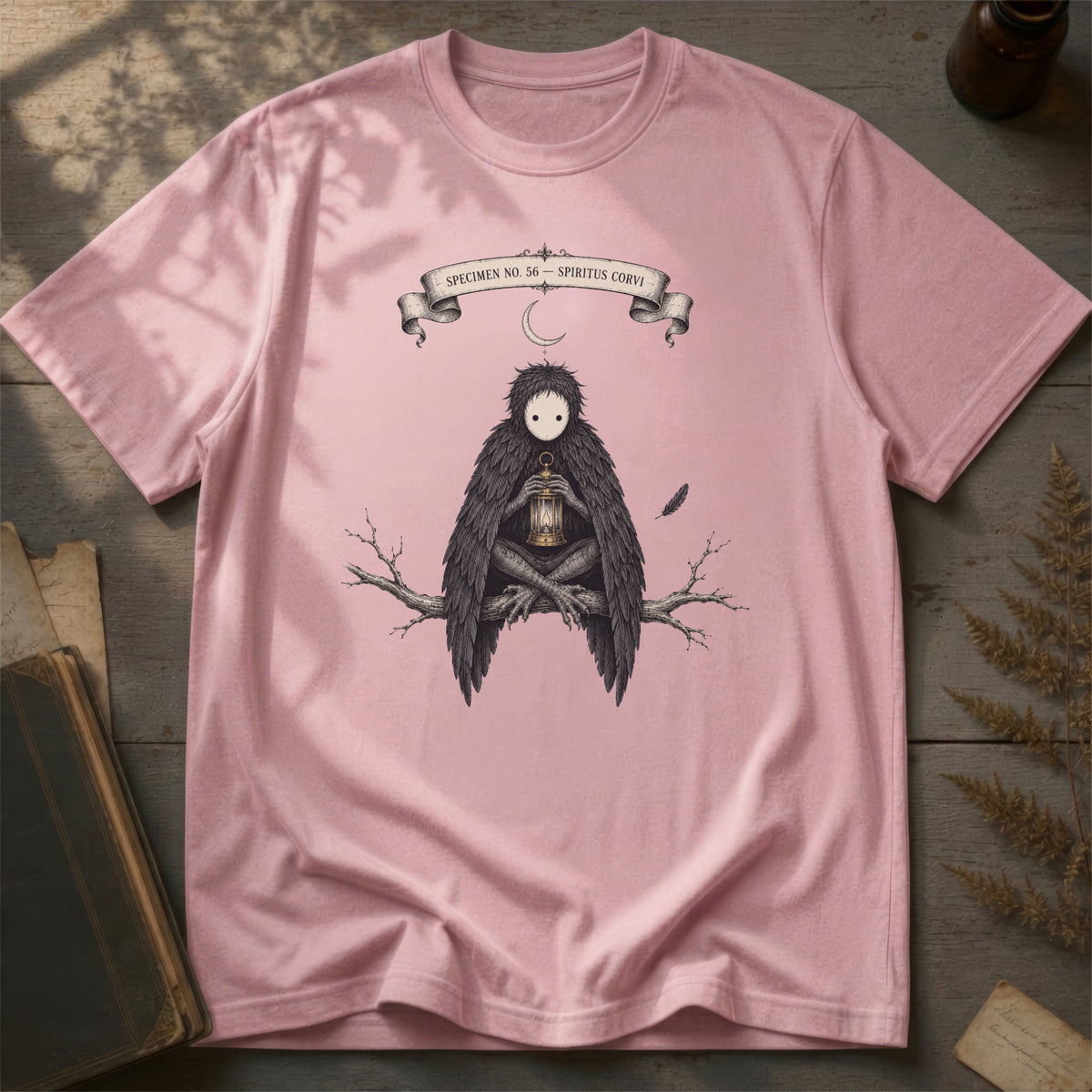 Orchid pink t-shirt with a gothic illustration of a raven-winged spirit sitting on a bare branch, holding a glowing lantern, beneath a crescent moon banner reading Specimen No. 56.