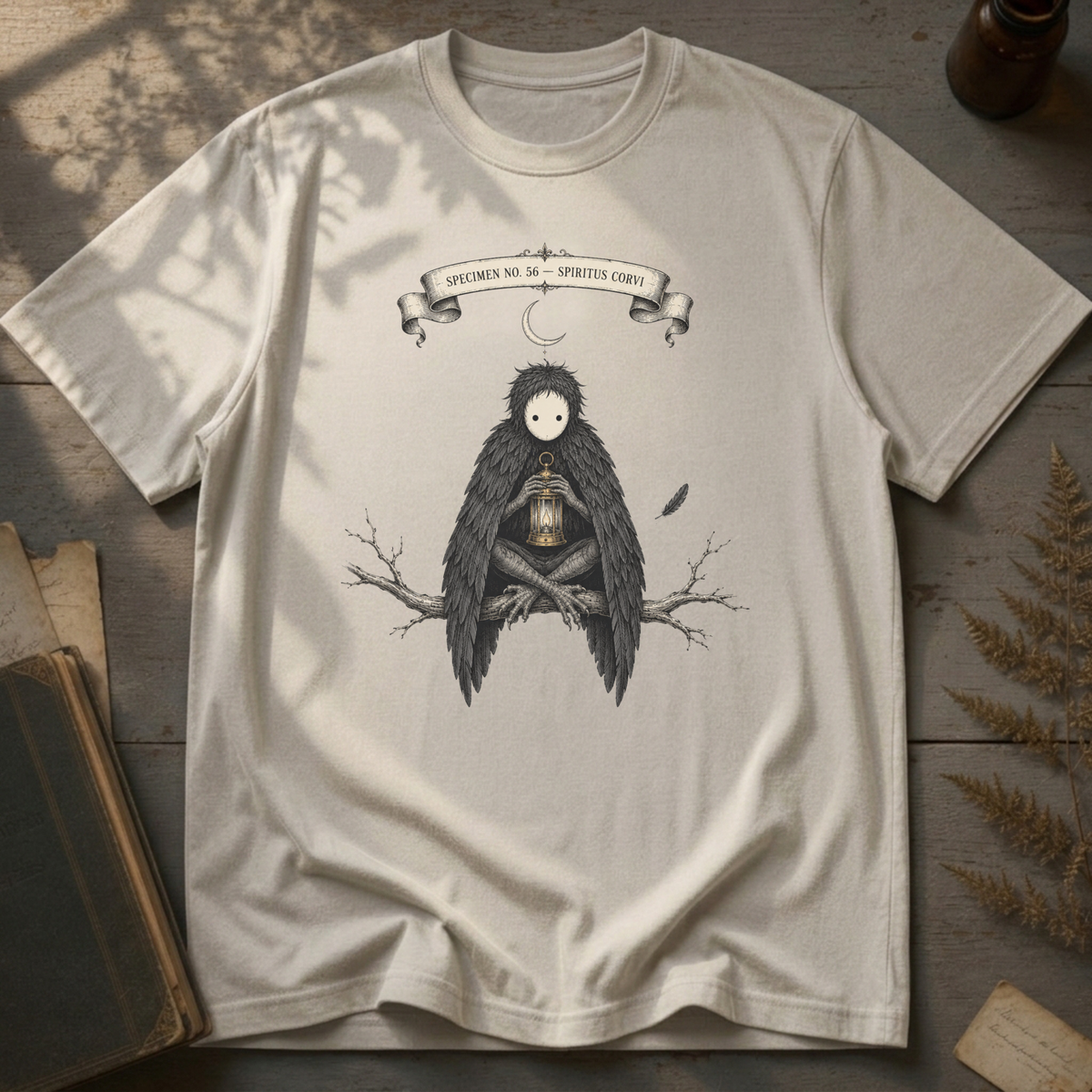 Vintage white t-shirt with a gothic illustration of a raven-winged spirit sitting on a bare branch, holding a glowing lantern, beneath a crescent moon banner reading Specimen No. 56.
