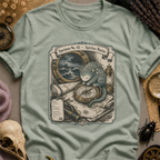 Sage green t-shirt with a sepia-toned illustration of a sea spirit resting a paw on a brass compass atop an antique nautical map, with a stormy porthole scene above.