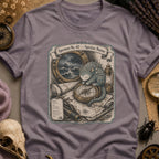 Storm grey t-shirt with a sepia-toned illustration of a sea spirit resting a paw on a brass compass atop an antique nautical map, with a stormy porthole scene above.