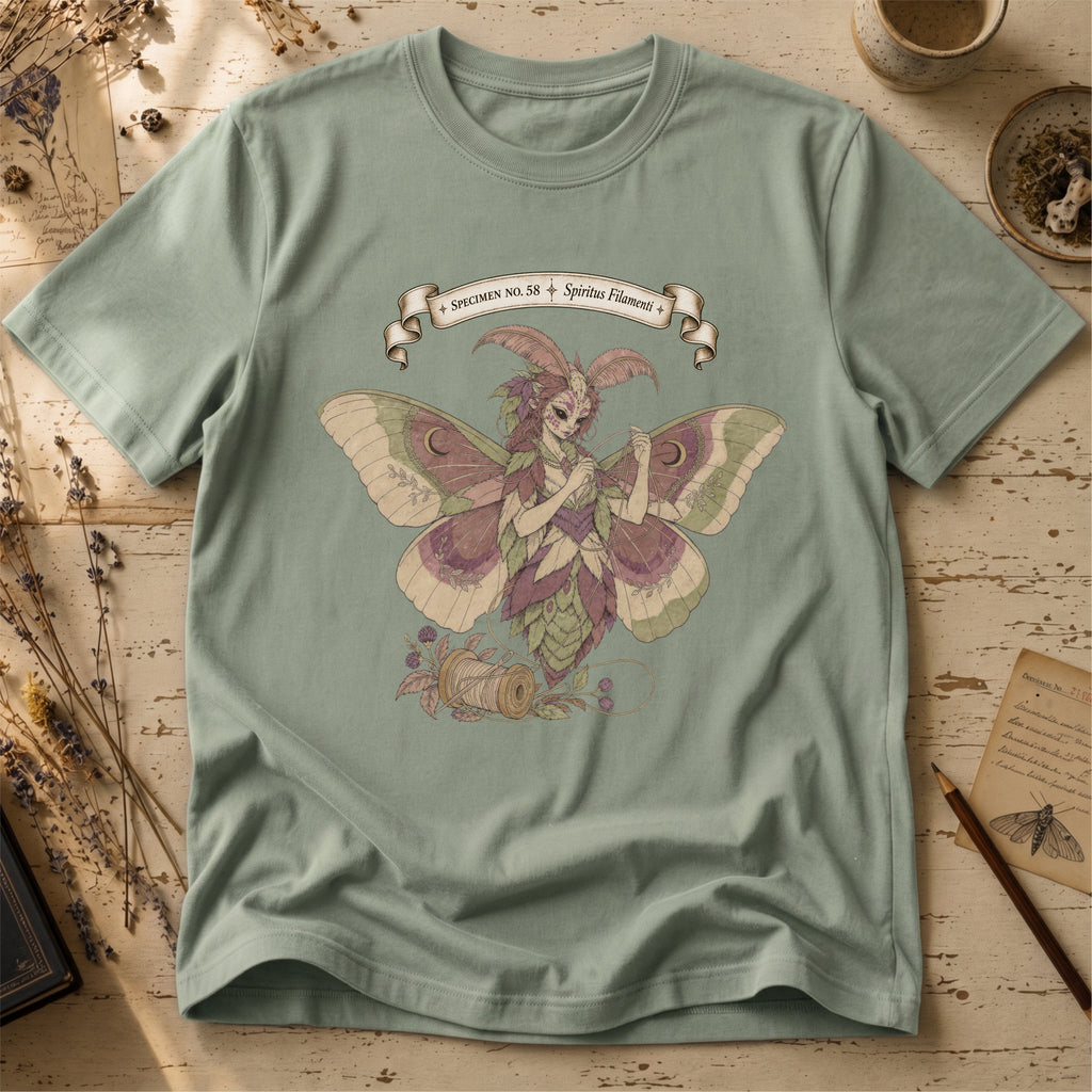 Sage green t-shirt with an illustration of a moth-winged spirit holding a strand of gold thread beside a spool and needle, surrounded by dusty pink flowers and sage leaves, beneath a banner reading Specimen No. 58.