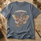 Steel blue t-shirt with an illustration of a moth-winged spirit holding a strand of gold thread beside a spool and needle, surrounded by dusty pink flowers and sage leaves, beneath a banner reading Specimen No. 58.